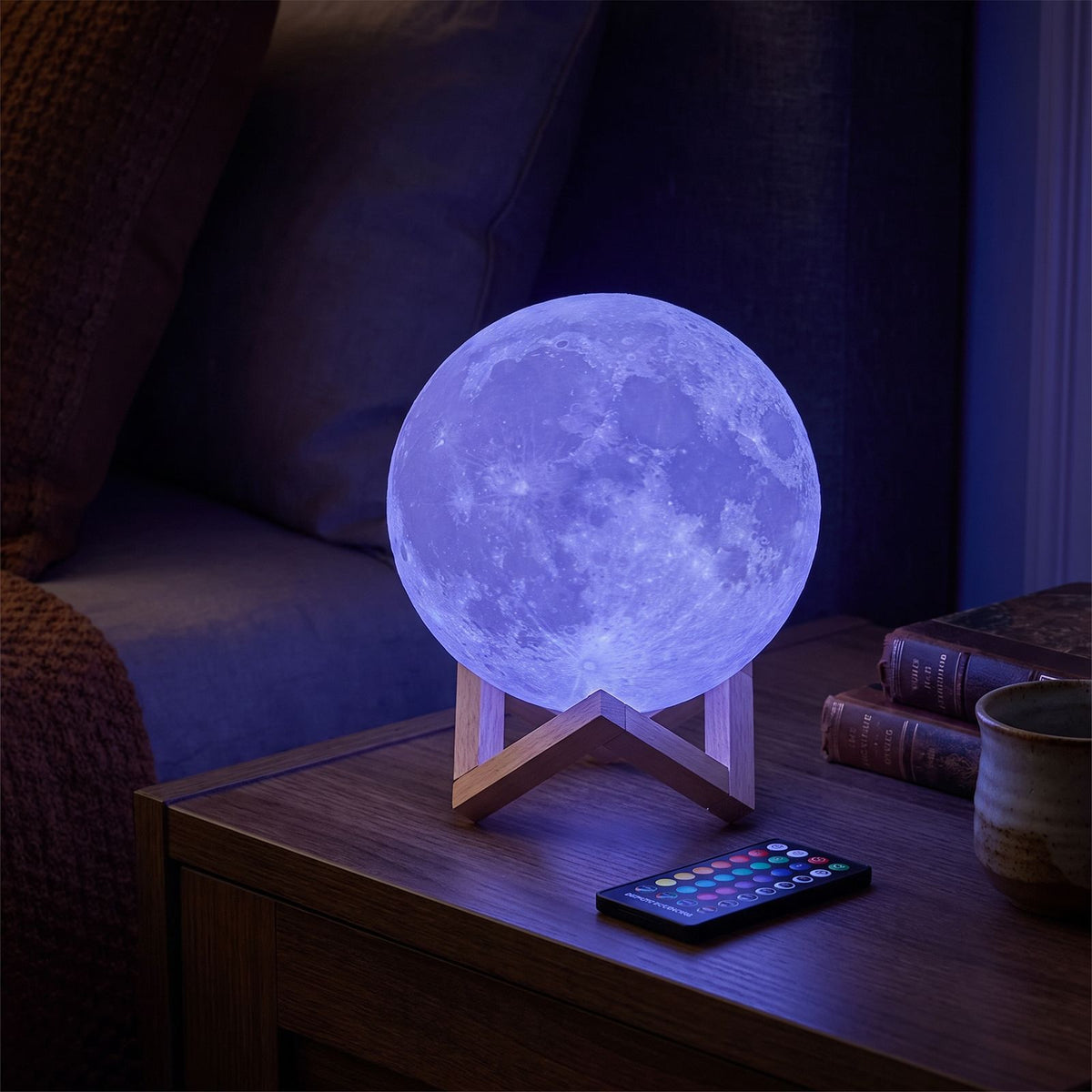 The 3D moon lamp glowing blue beside its remote control on a bedside table in a bedroom at night