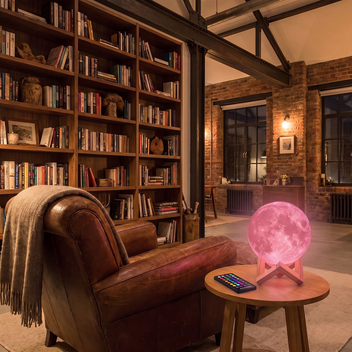 The 3D moon lamp glowing pink with its remote control on a side table beside a leather armchair in a living room reading corner