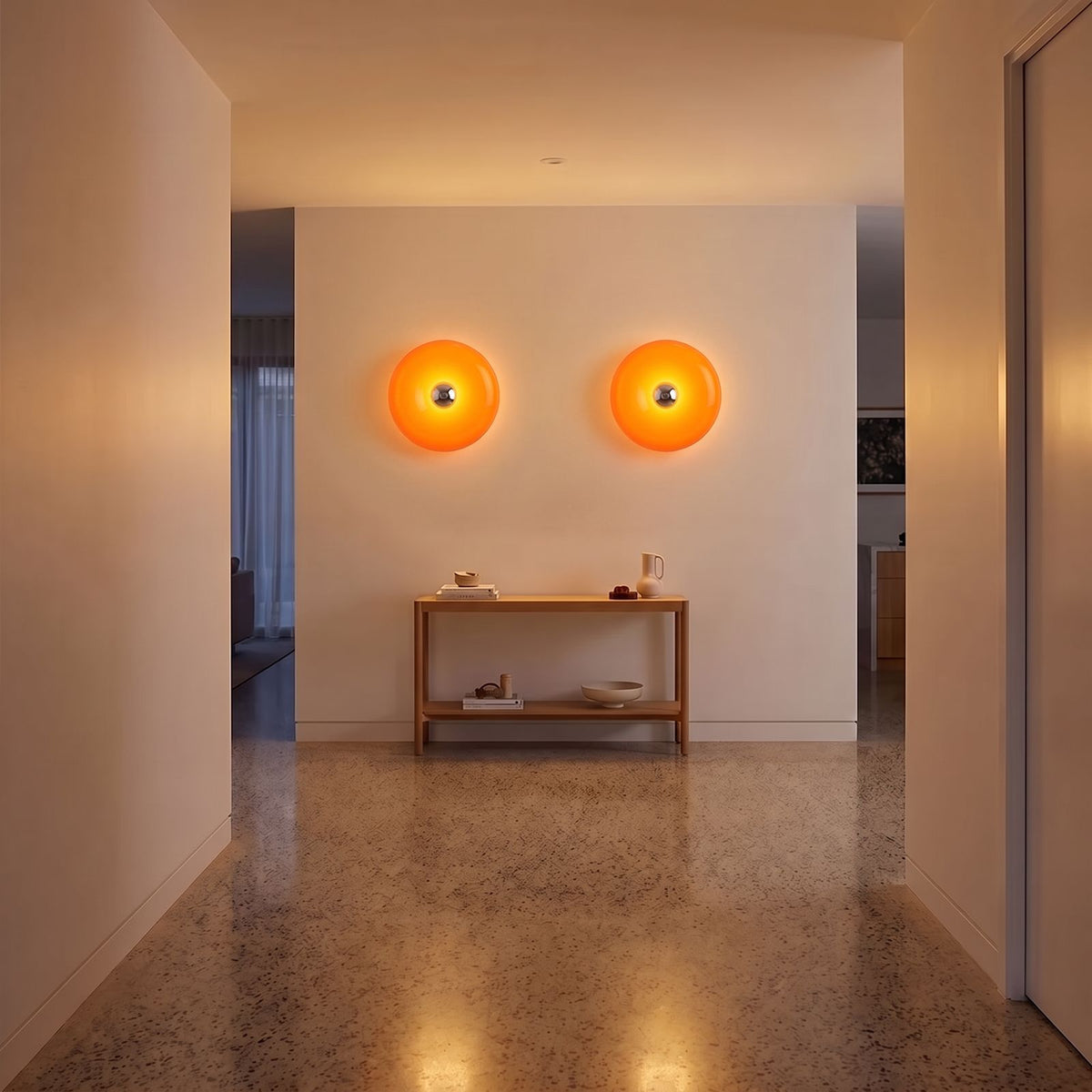 Pair of orange acrylic donut lamps on a hallway wall above a console in the evening
