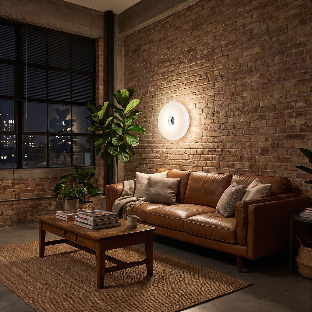 White acrylic donut lamp hung on a brick wall beside a sofa in a loft living room at night