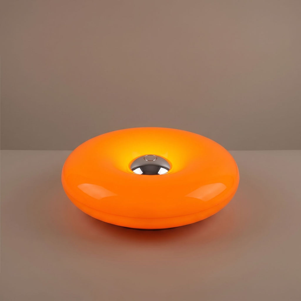 Close view of the orange acrylic donut lamp and its chrome centre button, switched on