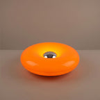 Close view of the orange acrylic donut lamp and its chrome centre button, switched on