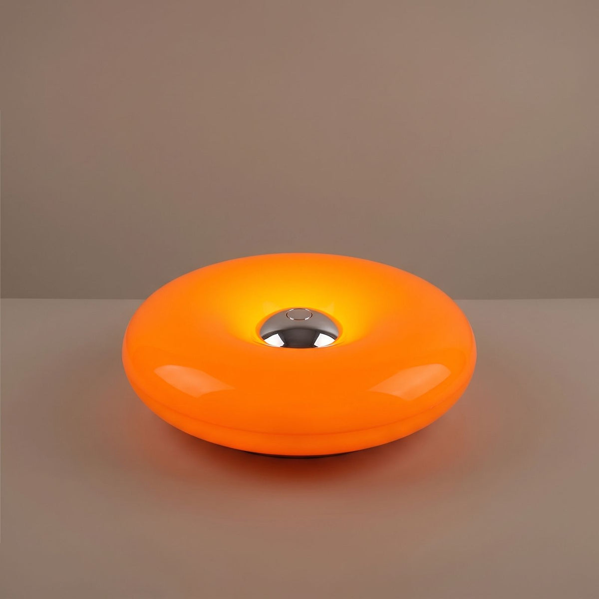 Close view of the orange acrylic donut lamp and its chrome centre button, switched on