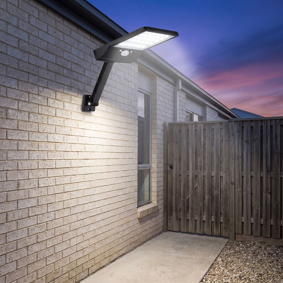 Adjustable Arm Remote Control Solar Sensor Wall Light on a brick wall beside a side gate at dusk