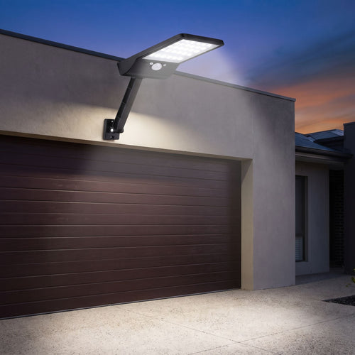 Solar sensor wall light on an adjustable arm above a garage door at dusk
