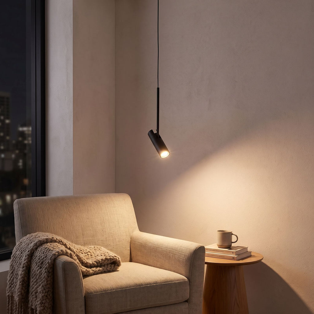 Black cylinder spotlight pendant light over an armchair in a reading corner