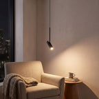 Black cylinder spotlight pendant light over an armchair in a reading corner