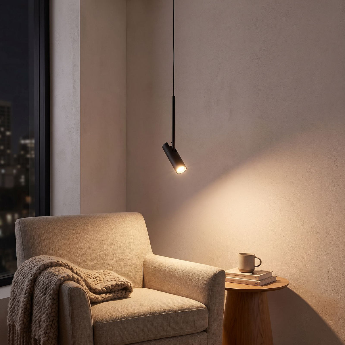 Black cylinder spotlight pendant light over an armchair in a reading corner