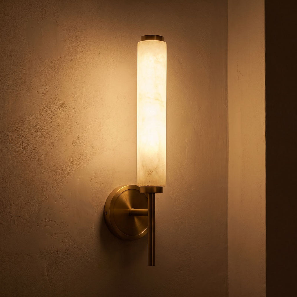 Alabaster Candle Brass Wall Sconce glowing on a plaster wall at night