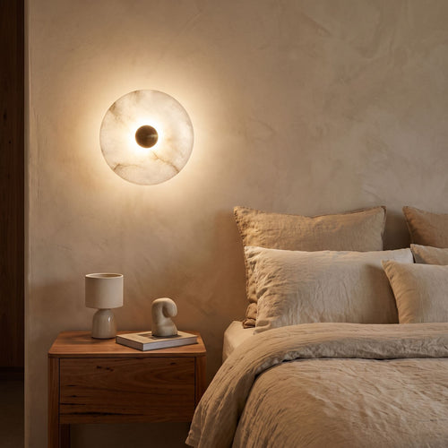 Alabaster Disc Wall Light beside a bed with linen bedding