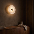 Alabaster Disc Wall Light glowing on a plaster wall at night