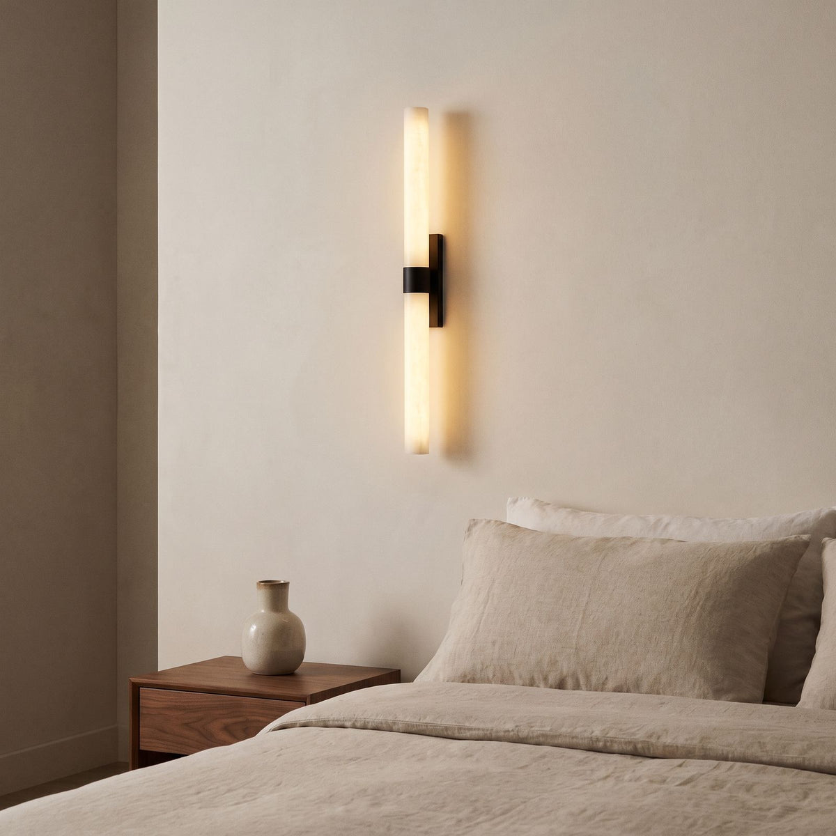 Alabaster Effect Cylinder LED Wall Light in matte black mounted beside a bed in a warm neutral bedroom
