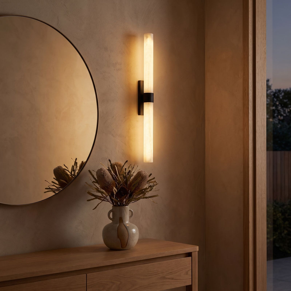 Alabaster effect cylinder wall light beside a round mirror in an entry hall