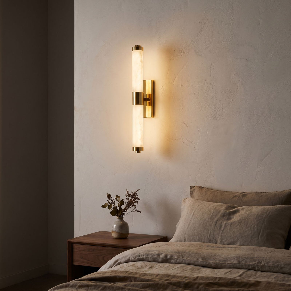 Alabaster Effect Cylinder LED Wall Light with polished gold bracket beside a bed