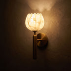Marble Flower Petal Brass Wall Sconce glowing on a plaster wall at night