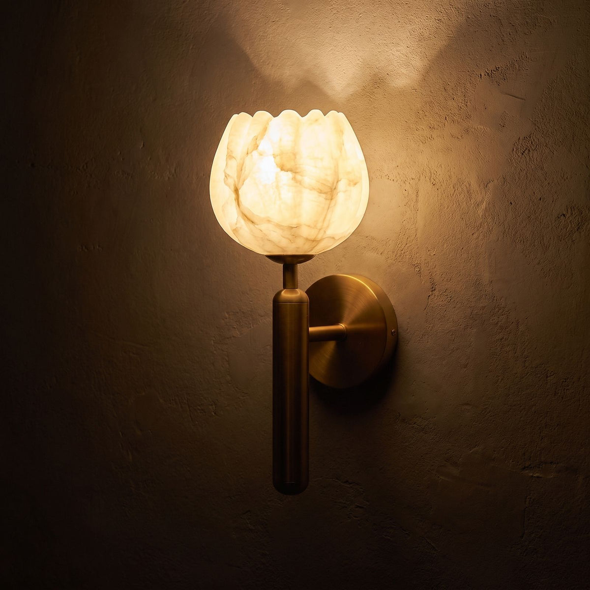 Marble Flower Petal Brass Wall Sconce glowing on a plaster wall at night