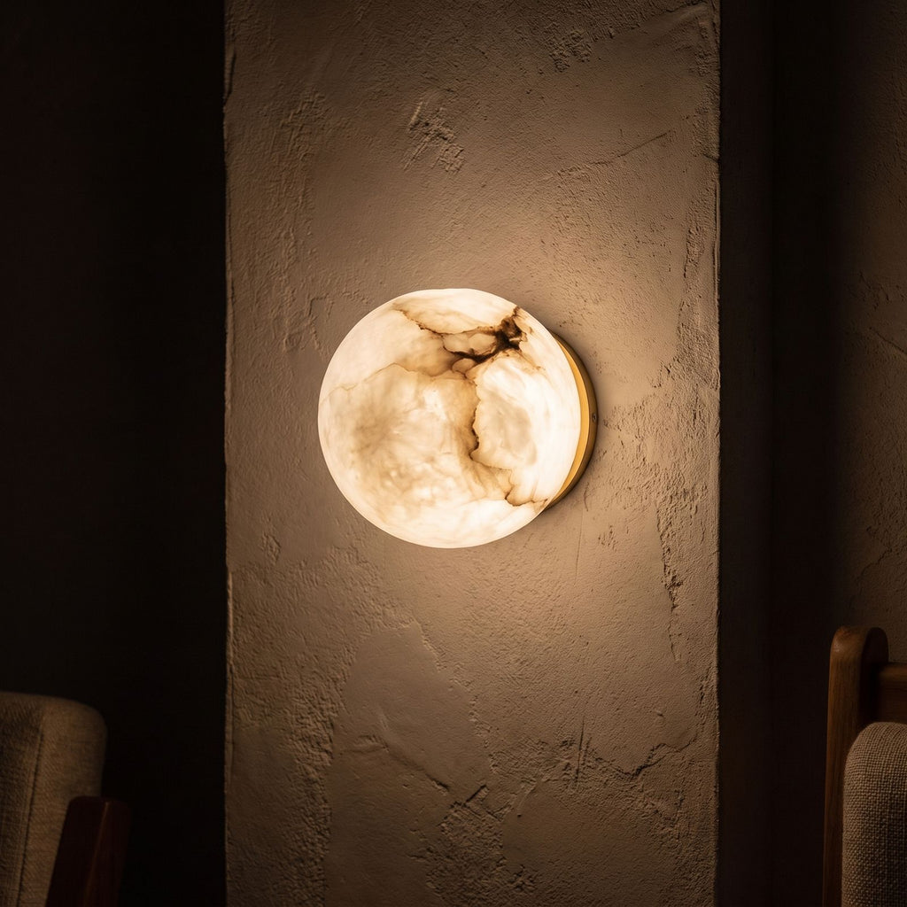 Alabaster Orb Wall Light with Gold Base glowing on a plaster wall at night