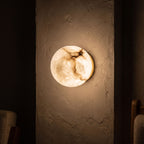Alabaster Orb Wall Light with Gold Base glowing on a plaster wall at night