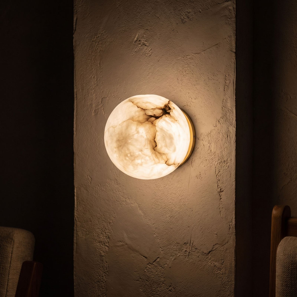 Alabaster Orb Wall Light with Gold Base glowing on a plaster wall at night
