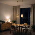 Two amber glass capsule pendants above a round oak dining table in an apartment at night