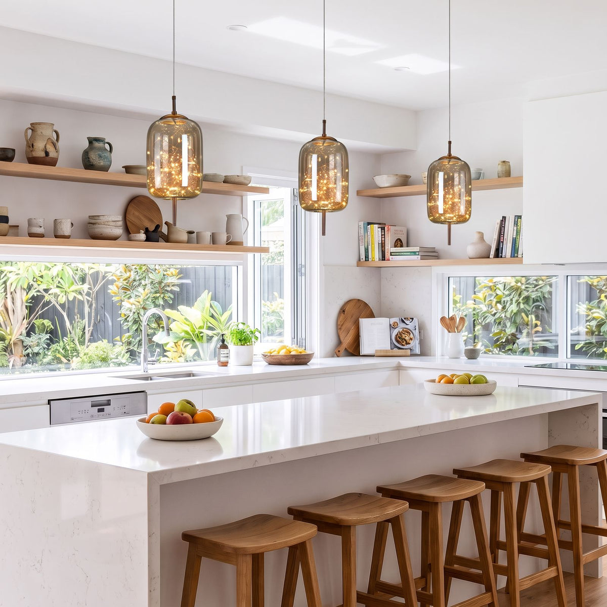 Three amber glass capsule pendants in a row above a white stone kitchen island in a coastal home by day