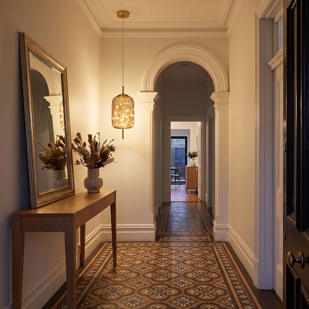 The amber glass capsule pendant above a console in a heritage entry hallway in the evening