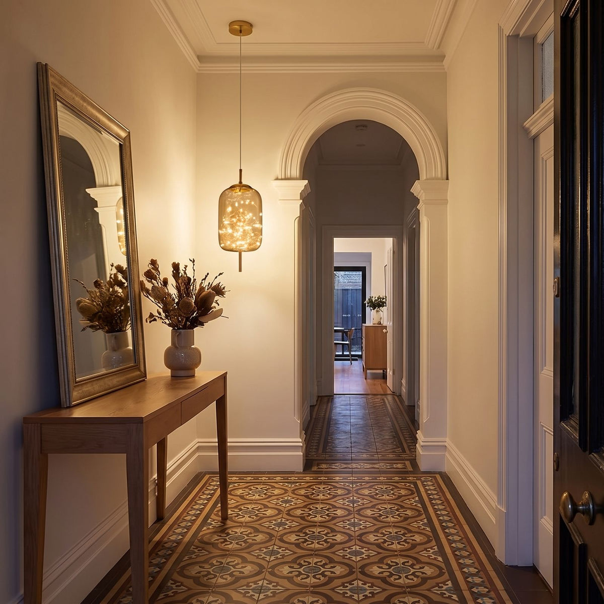 The amber glass capsule pendant above a console in a heritage entry hallway in the evening