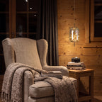 The amber glass capsule pendant above a side table beside an armchair in a timber cabin reading corner at night