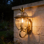 Antique Brass Glass Outdoor Wall Lantern glowing on a limestone garden wall at night