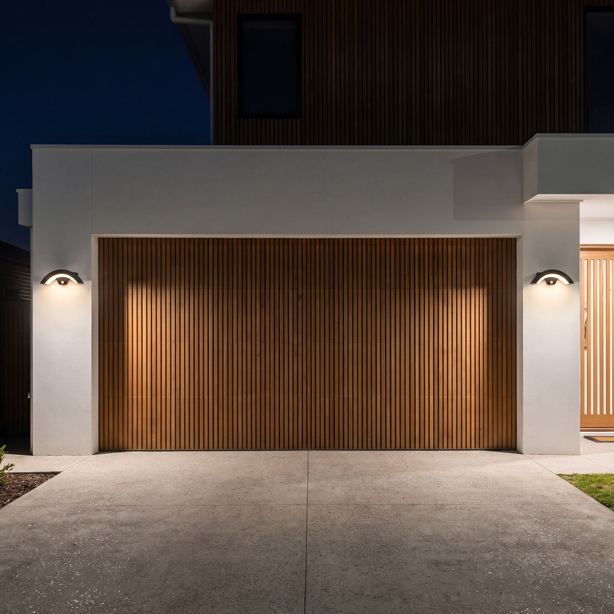Two Arc Motion Sensor Outdoor Wall Lights either side of a timber batten garage door at night