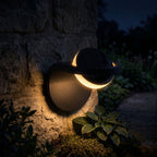 Arched Metal and Acrylic Outdoor Wall Light glowing on a garden wall at night