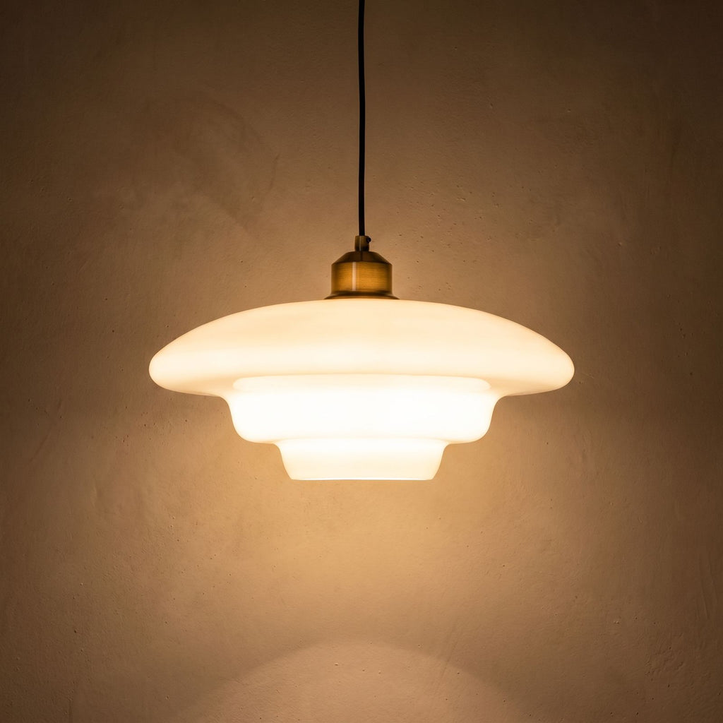 Art Deco Tiered Glass and Brass Pendant Light glowing against a plaster wall at night