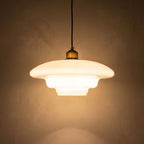 Art Deco Tiered Glass and Brass Pendant Light glowing against a plaster wall at night