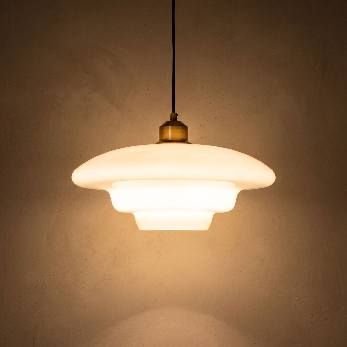 Art Deco Tiered Glass and Brass Pendant Light glowing against a plaster wall at night
