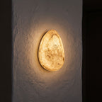 Backlit Floating Pebble Marble Wall Light glowing on a plaster wall at night
