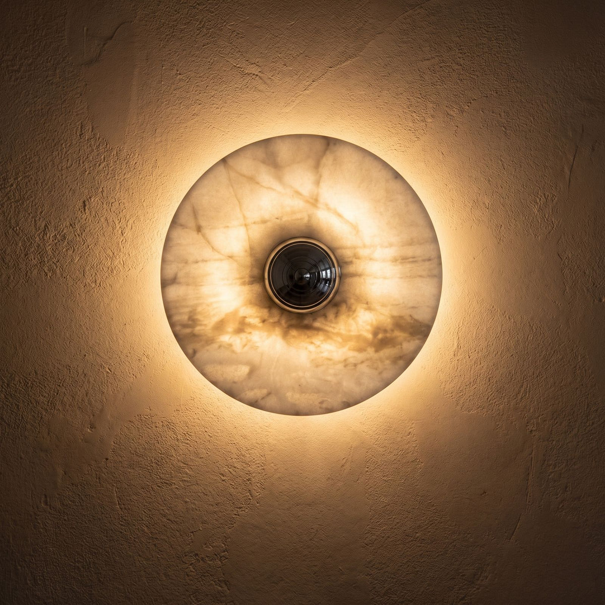 Backlit Marble Disc Touch Wall Light glowing on a plaster wall at night