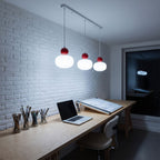 Ball-top scalloped acrylic 3-light pendant lit in cold white above a long studio workbench at night