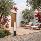 Black Aluminium Cylinder White Diffuser LED Bollard Light in a courtyard gravel bed in daylight