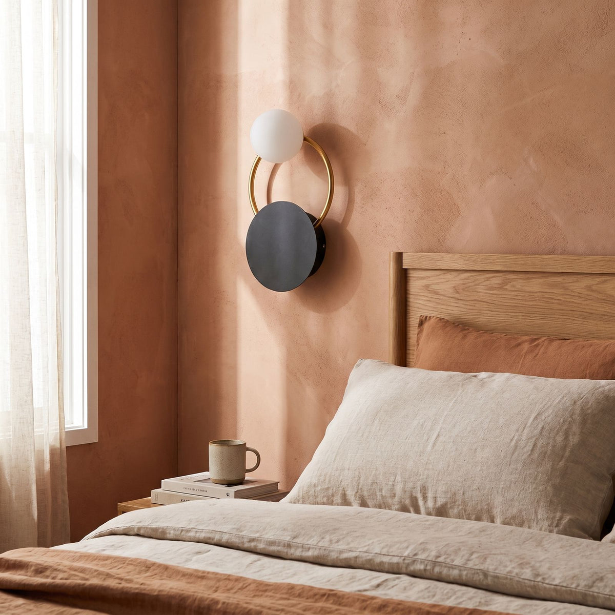 Black Disc, Gold Ring and Glass Orb Wall Light on a bedroom wall beside the bed