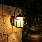 Black Iron and Amber Glass Outdoor Wall Light glowing on a garden wall at night
