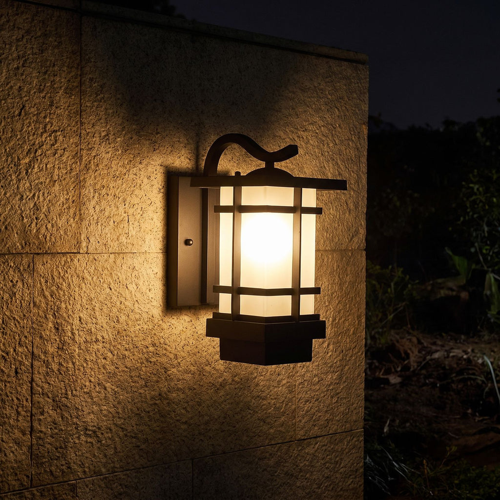Black Iron and Frosted Glass Outdoor Wall Lantern glowing on a garden wall at night