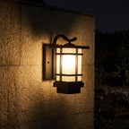 Black Iron and Frosted Glass Outdoor Wall Lantern glowing on a garden wall at night