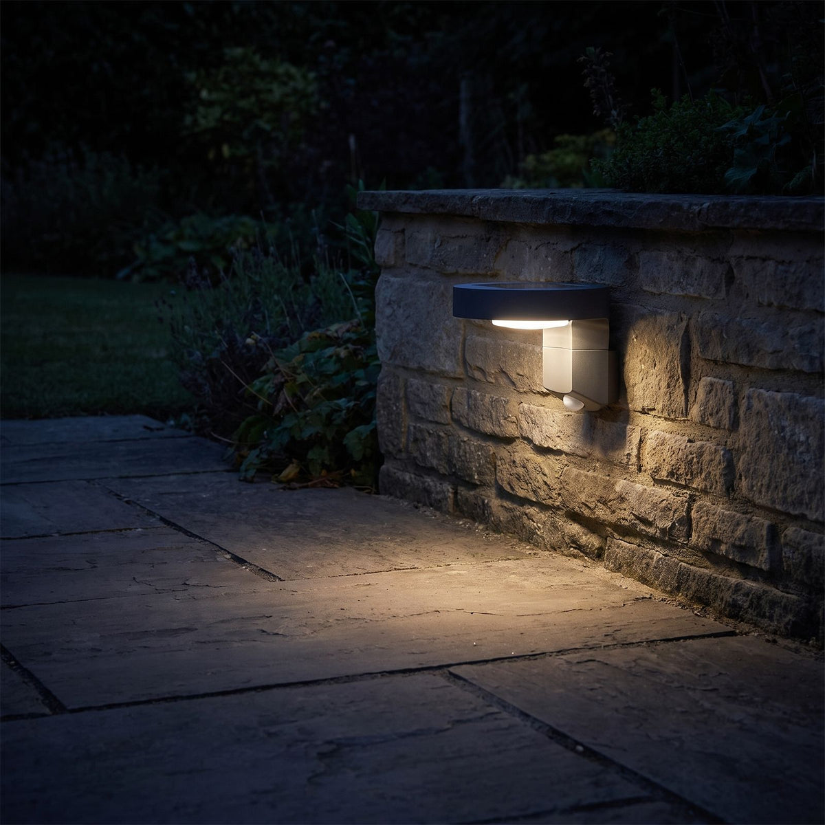 Black Metal and Acrylic Solar Sensor Wall Light glowing on a garden wall at night