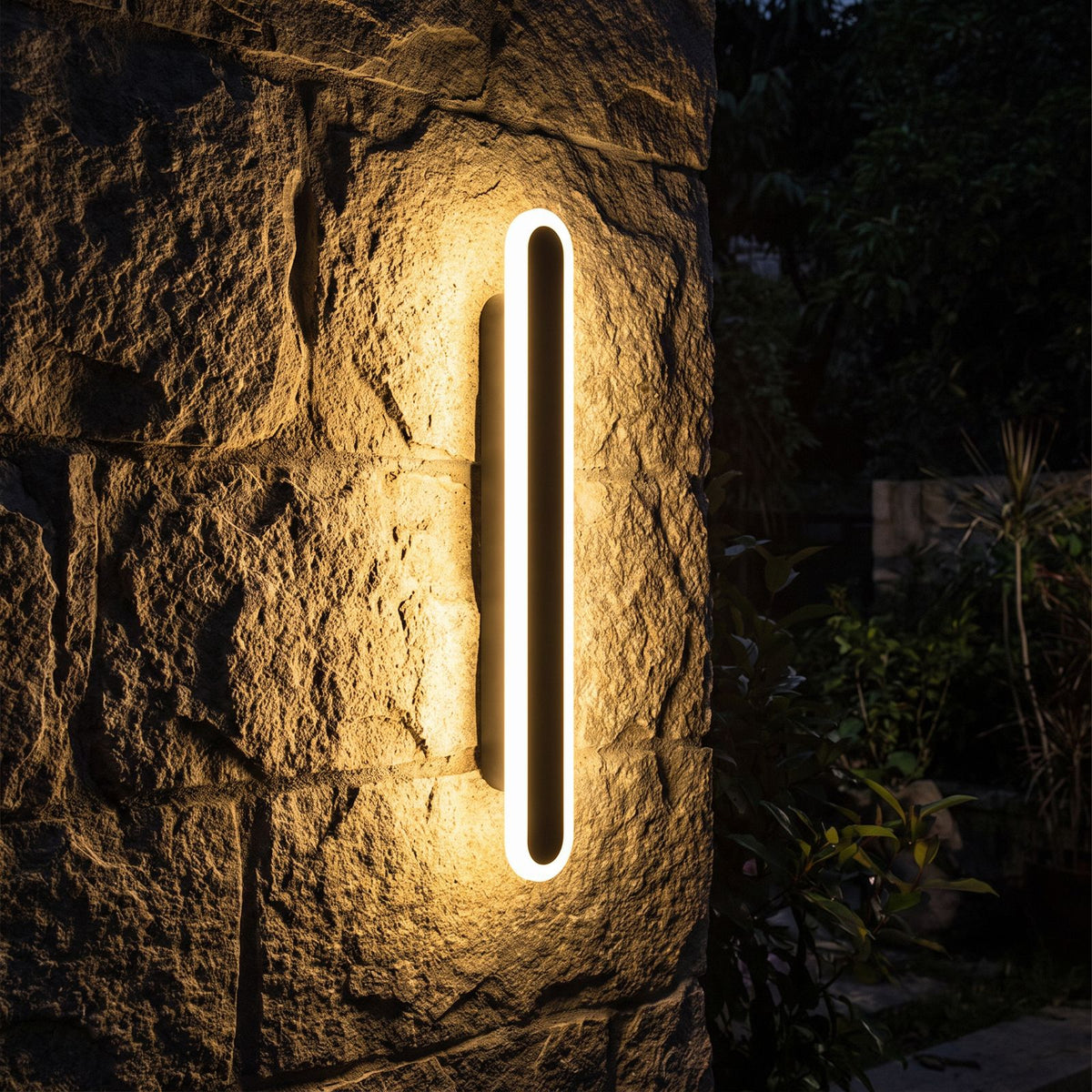 Black Oval Linear LED Outdoor Wall Light glowing on a garden wall at night