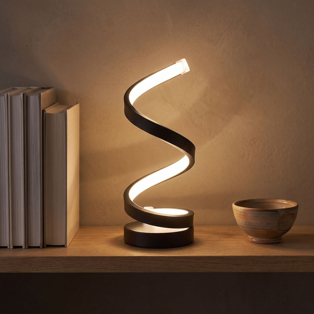Black spiral ribbon table lamp on an oak shelf beside books