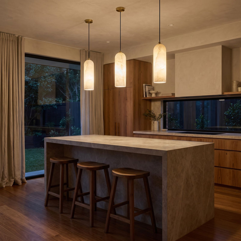 A row of three Brass and Alabaster Capsule Pendant Lights over a stone kitchen island