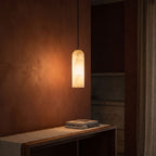 Brass and Alabaster Capsule Pendant Light glowing against a plaster wall at night