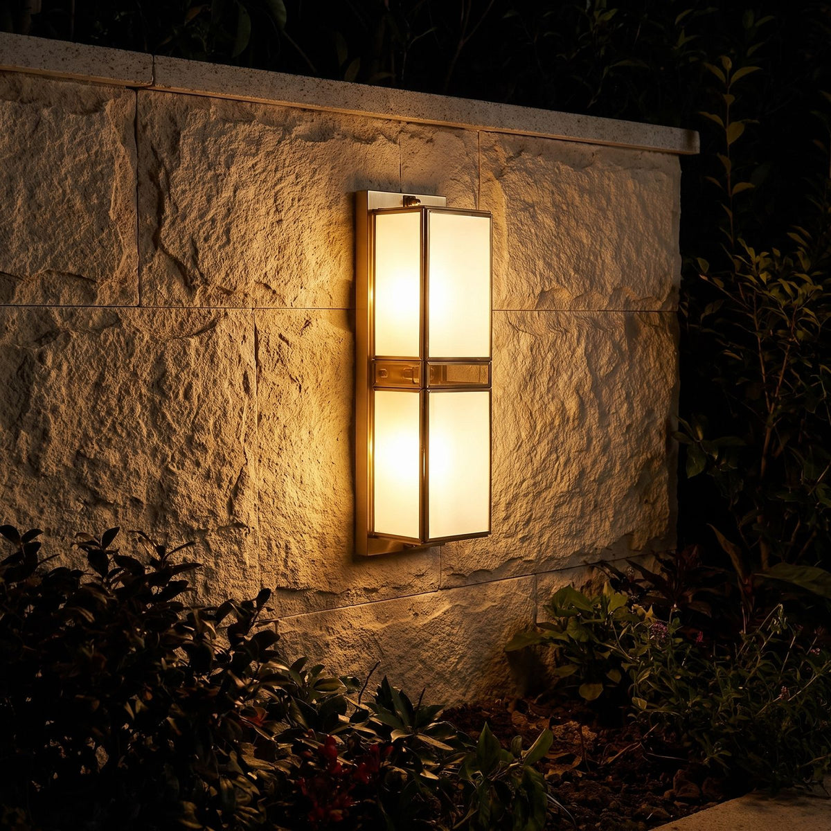 Brass and White Glass Outdoor Wall Light glowing on a garden wall at night
