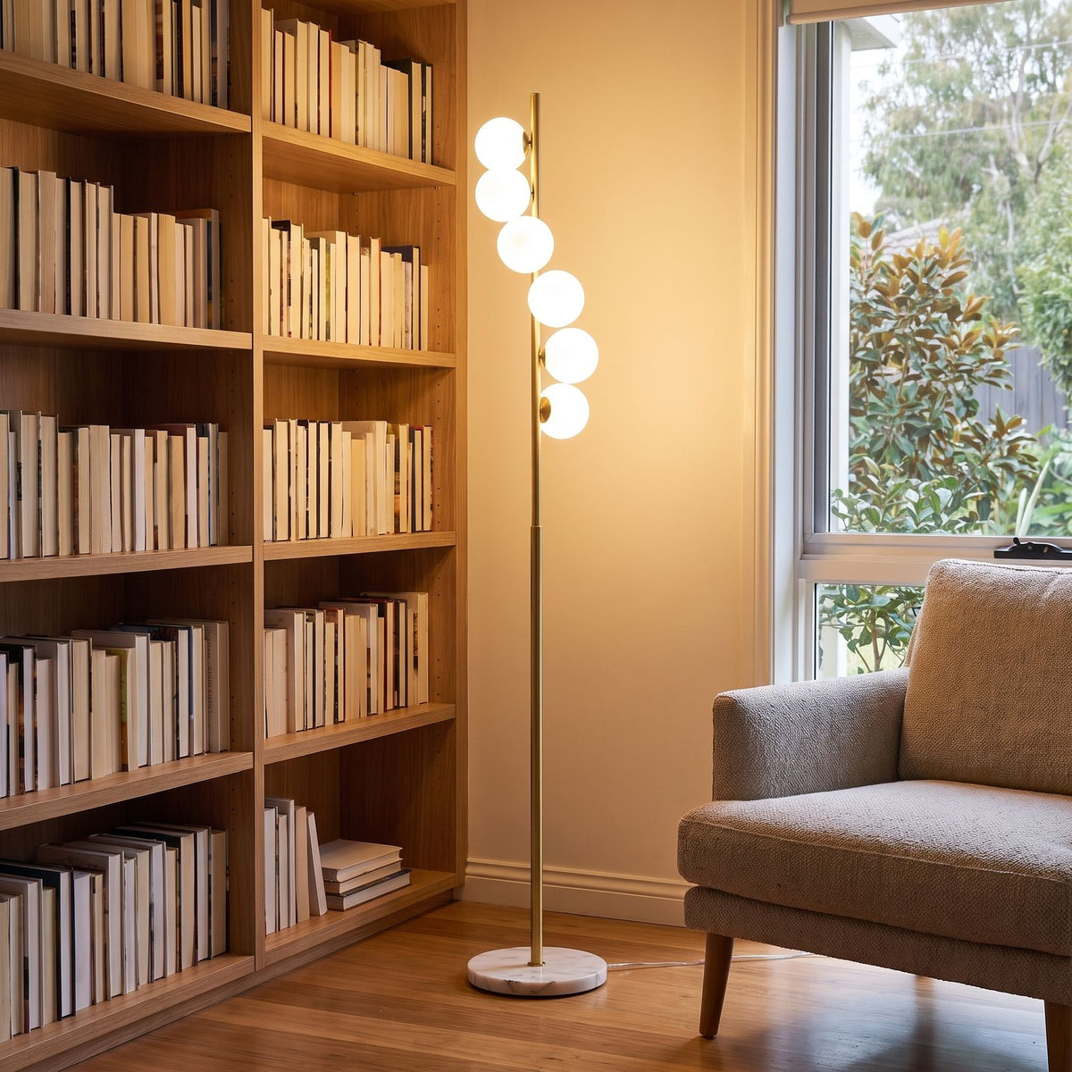 Brass finish opal glass globe floor lamp in a reading corner beside a bookshelf