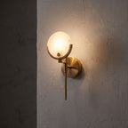 Brass Rod Alabaster Globe Wall Light glowing on a plaster wall at night